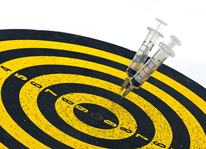 Two medical syringes stuck in a darts board, missing the bullseye